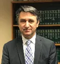 Portrait of Dimitrios Ioannidis in a dark suit, photographed in front of shelves of law reports