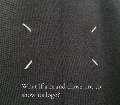 Close-up of dark fabric showing Maison Margiela’s four white stitches, overlaid with the line “What if a brand chose not to show its logo?”