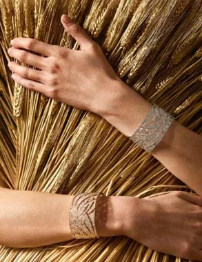 Two wrists wearing diamond wheat-motif cuffs against a background of gold wheat stalks