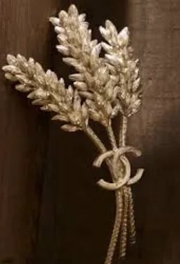 A gold wheat-ear brooch with Chanel’s interlocking CC monogram at its base, on dark wood